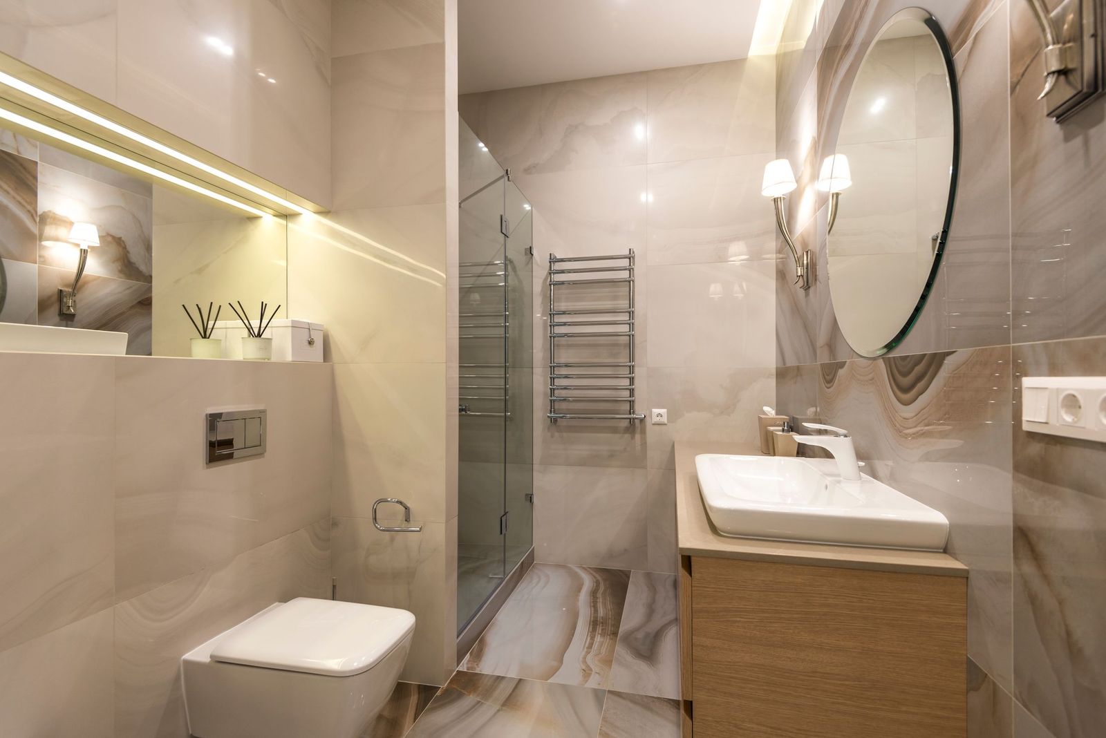 Warm beige ensuite with a glass shower, round mirror and timber vanity